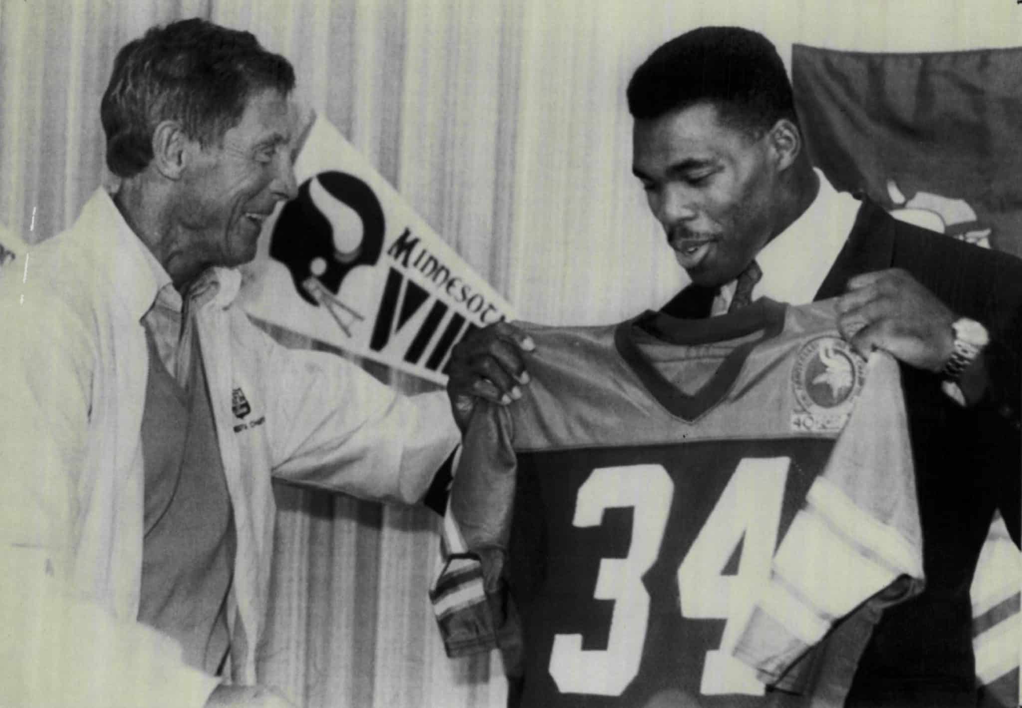 MINNEAPOLIS, MN - CIRCA 1989: Minnesota Vikings coach Jerry Burns greets Herschel Walker #34 of the Minnesota Vikings as Walker holds up his Vikings' jersey during a 1989 press conference after Walker was traded by the Dallas Cowboys to the Vikings in Minneapolis, Minnesota. Walker played for the Vikings form 1989-91.